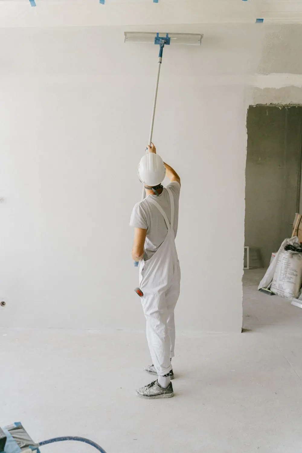 Schilder in witte overall rolt een plafond in een lege witte ruimte